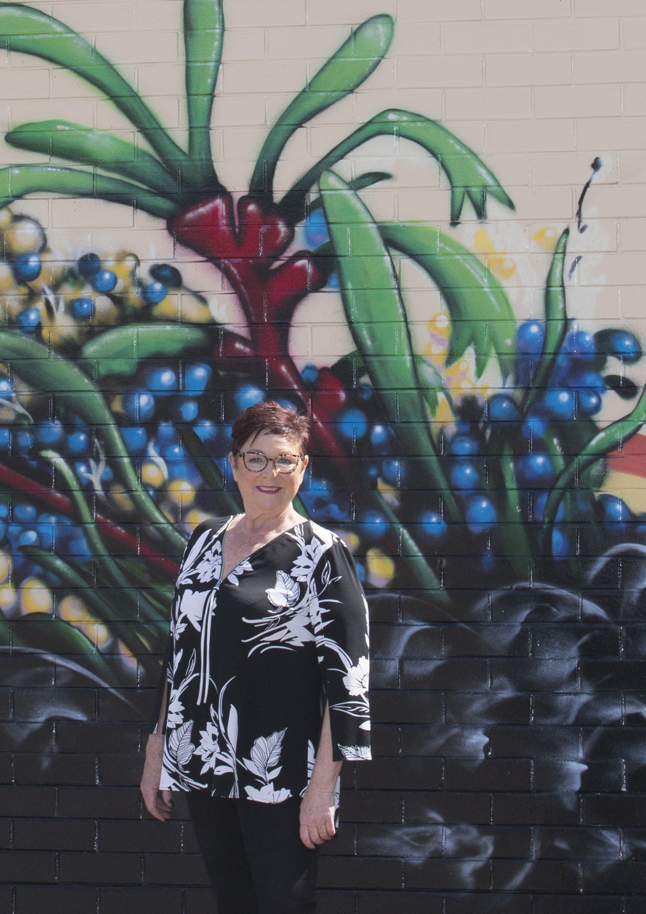 Lisa Baker MLA with street art in background. Art is of Red Kangaroo Paw and part of a Black Swan
